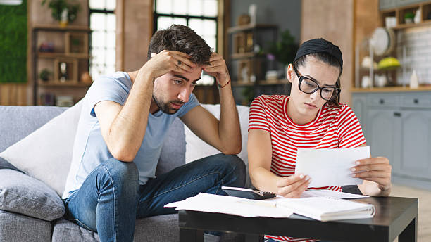 istock Couple calculating bills at home using tablet and calculator. Young couple working on computer while calculating finances sitting on couch. Young man with wife at home analyzing their finance with documents. 2240546594