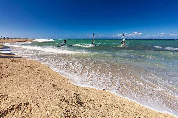 Aerial shot of an older man windsurfing across calm, clear blue waters. Captured from directly above, the image highlights the vibrant sail, the movement of the board, and the expansive beauty of the open sea. The man appears active and focused, embodying adventure, vitality, and freedom. Ideal for themes of healthy aging, sports, lifestyle, travel, and outdoor recreation. Taken near Pag Island, Croatia in the Adriatic Sea.