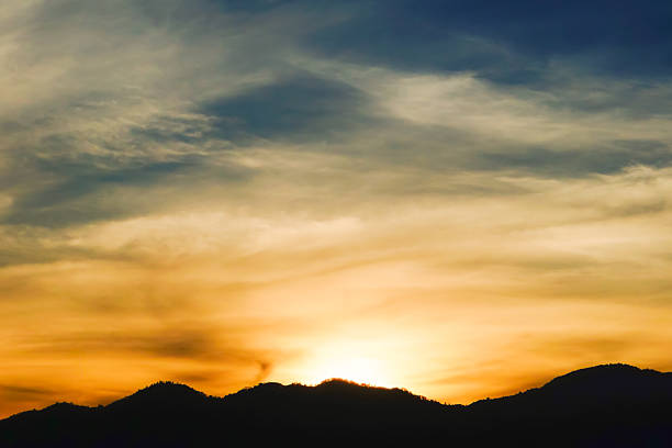 Scenic mountain silhouette at sunset with dramatic golden sky and soft clouds. This peaceful twilight landscape captures the beauty of nature, perfect for backgrounds, travel, or relaxation themes.