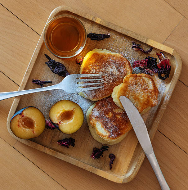 Delicious homemade breakfast in flat lay style featuring pancakes sprinkled with powdered sugar, a cup of tea, and fresh plums. Perfect for illustrating cozy mornings, slow living, healthy food, and home lifestyle concepts.