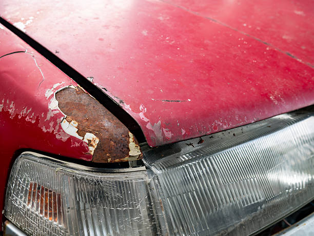 Severe rust corrosion and peeling paint damage on red car hood edge above headlight showing metal deterioration