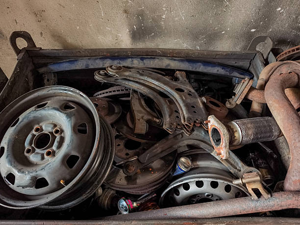 Rusty car parts, including wheels, exhaust pipes, and suspension components, fill a metal bin in a garage, highlighting automotive repair and disposal
