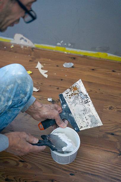 Man preparing wall filler with spatulas during home renovation work indoors