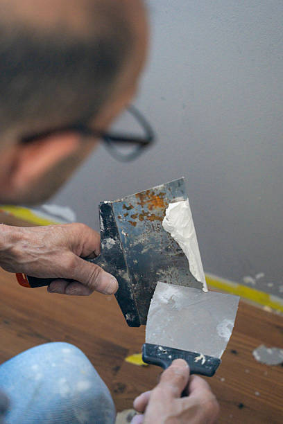 istock Man preparing wall filler with spatulas during home renovation work indoors 2240563579