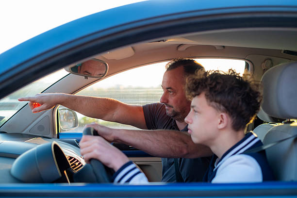 istock Father teaching son driving a car at sunset 2240564282