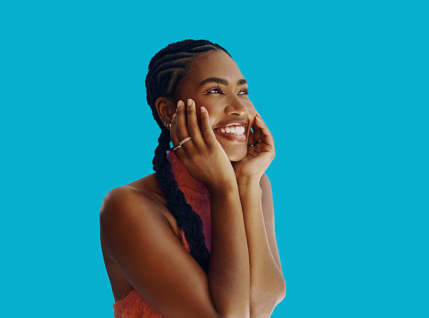 Smiling Black woman with braided hair and rings against a vibrant blue background radiates happiness and calm. Her joyful, blissful expression highlights warmth and serenity in this close-up portrait.