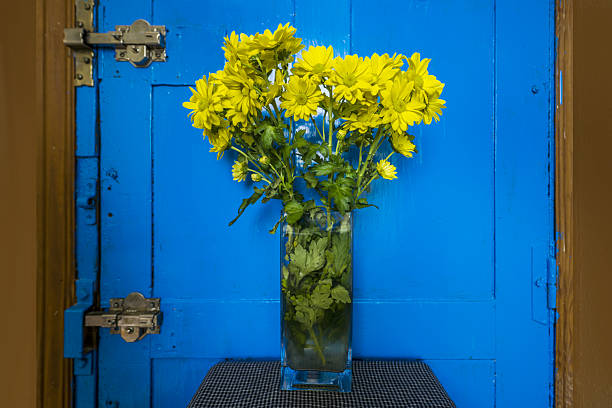 A vase of yellow daisies next to a bright blue door