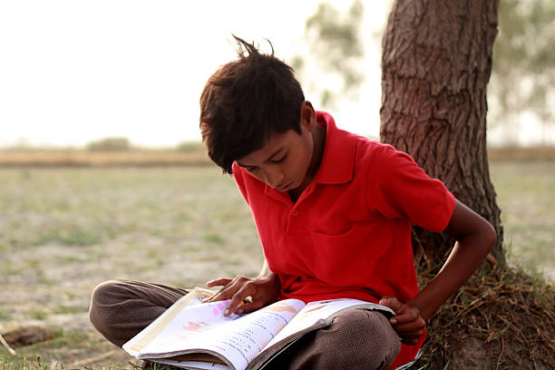 istock Poor Child Reading Book Outdoors in Nature in Rural Setting 2240571228