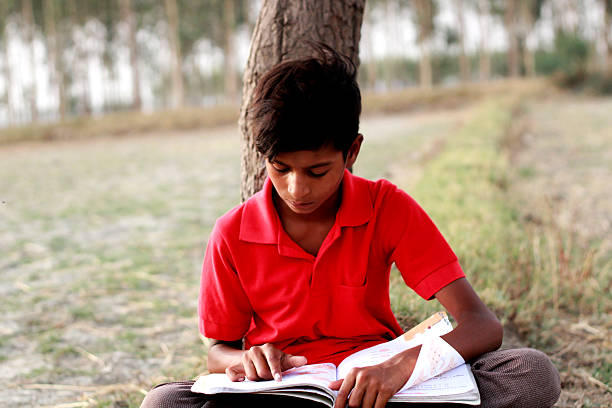istock Young Boy Reading school book While Leaning Against Tree Outdoors in Quiet rural Setting 2240571247