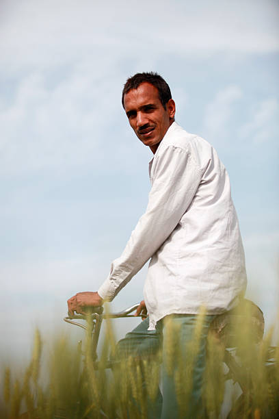 A man rides a bicycle through a sunlit field, wearing a white shirt. The bright sky and shallow depth of field create a calm, outdoorsy mood suitable for lifestyle, travel, and wellness themes.