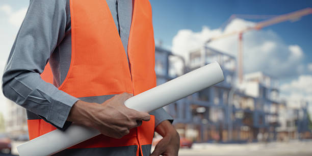 istock Construction Worker with Blueprint in Orange Safety Vest Outdoors 2240584818