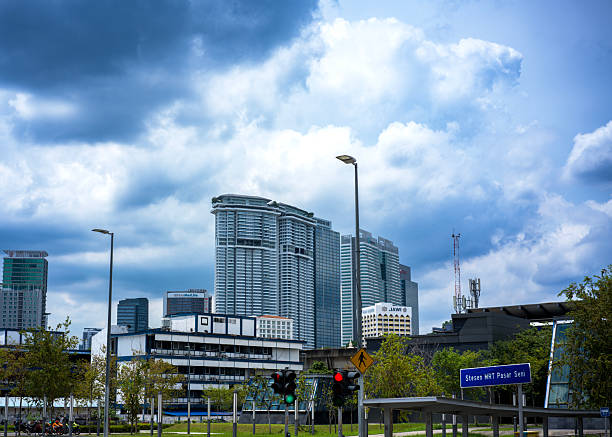 A dynamic view of Kuala Lumpur’s modern skyline featuring glass skyscrapers and the MRT Pasar Seni transit sign under dramatic cloudy skies.