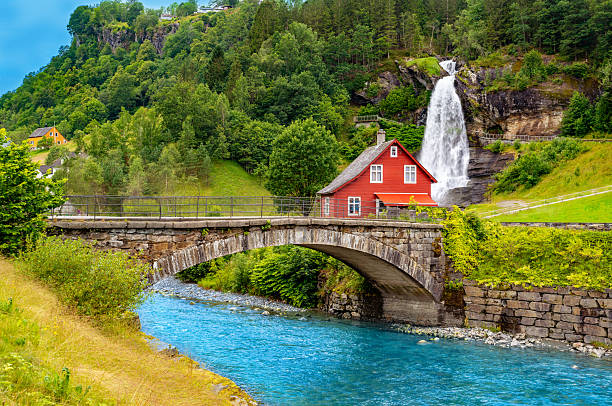Steinsdal arch bridge and red wooden house beside Steinsdalsfossen waterfall in summer Norway near Hardangerfjord
