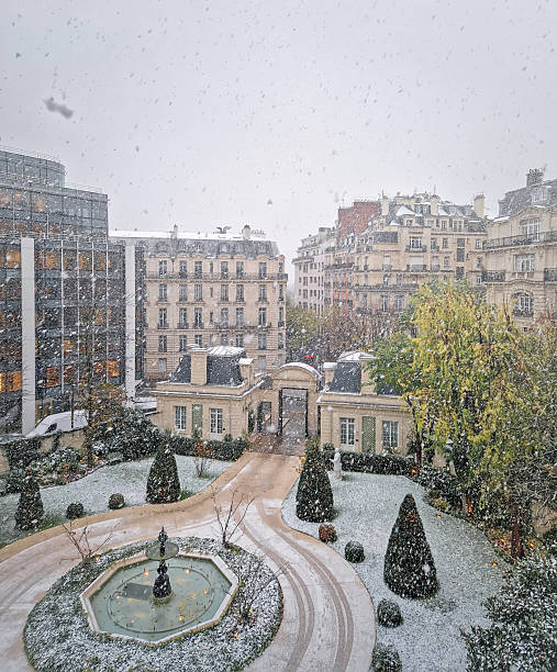 Peaceful Paris city view in a cold winter day during snowstorm with large flakes falling. Beautiful parisian old buildings covered in snow with view to a courtyard