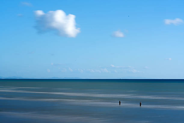 Captured with a Sing Ray 10-stop ND filter using long exposure, this image shows two fishermen standing in the sea. The smooth water surface and soft clouds create a calm, timeless atmosphere across the scene.