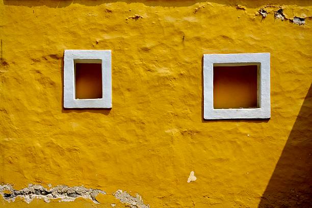 A close-up of an aging yellow church, with two white-framed square windows.