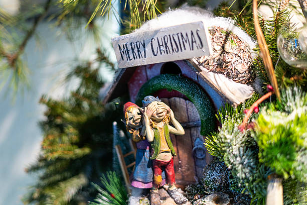A red square sign featuring the words 'Merry Christmas' in white script with star accents serves as the focal point, placed on a white faux fur surface. Surrounding it are fresh green fir branches (Abies species), brown pine cones (Pinus species), a woven wreath with berries, and twinkling white fairy lights draped around. Additional red ribbon and green holly leaves add to the arrangement. The composition evokes a joyful, warm holiday atmosphere suitable for winter celebrations. This image is ideal for commercial use in greeting cards, seasonal advertisements, blog illustrations for Christmas recipes or decor ideas, social media posts promoting holiday events, and editorial content on festive traditions by authors and media companies.