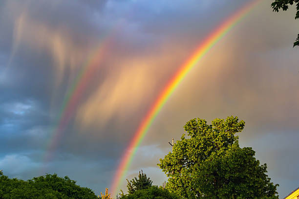 A double rainbow in the sky in rain clouds. A rainbow is an optical phenomenon caused by refraction, internal reflection and dispersion of light in water droplets resulting in a continuous spectrum of light appearing in the sky