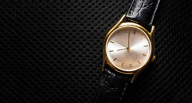 istock Women's wristwatch. Gold metal watch. Black fabric background pattern. Clock hands. Black leather strap. Time. 2240611280