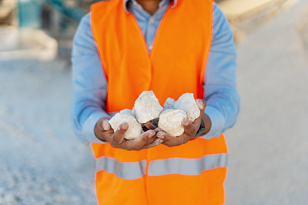 Quarry engineer wearing orange vest showing white stones in hands, close up. stone mining. Heavy industry concept