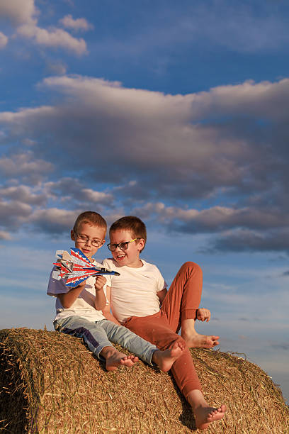 Two brothers sit on hay bale under blue sky, smiling and enjoying summer adventure. Concept for freedom, travel, and design with copy space.