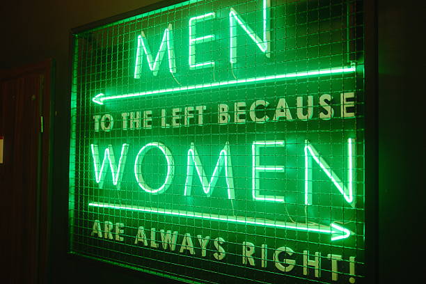A bright green neon sign displays gender-specific bathroom instructions with a joke.
