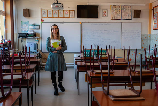 Professional female teacher standing in an empty school classroom with stacked chairs