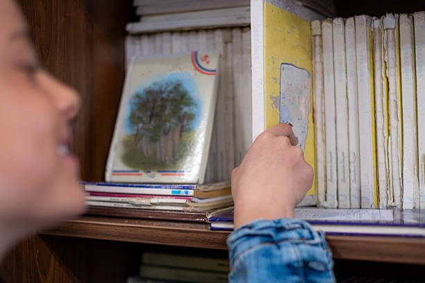 Young girl's hand selecting book from a dusty bookshelf, featuring cyrillic script