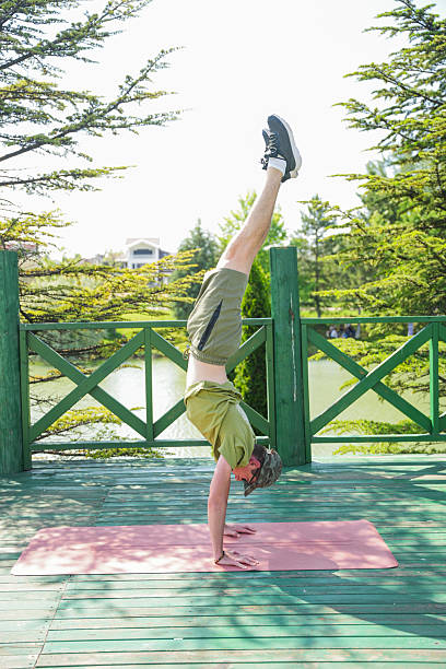 Man practicing handstand yoga pose outdoors on a pink mat in sunny park