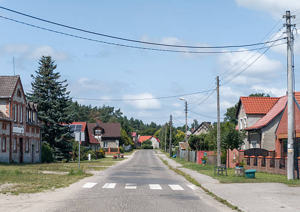 Village street in Poland with traditional houses, power lines, greenery, and blue summer sky—typical countryside residential scene