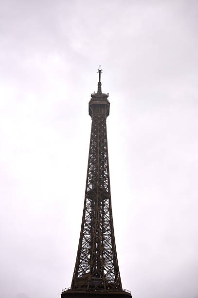 Eiffel tower's upper section against a stark, overcast parisian sky