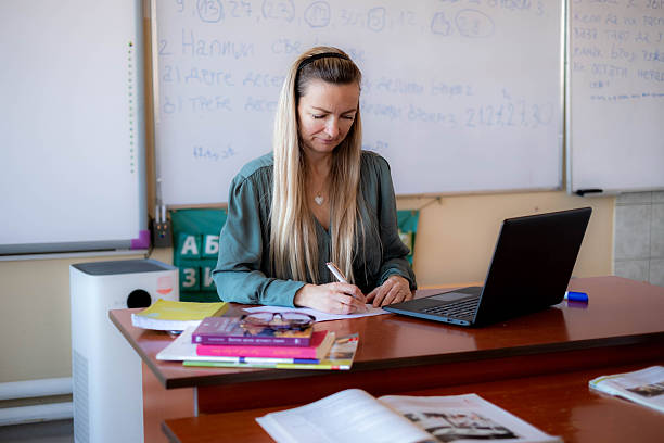 istock Woman teacher working in classroom writing on paper 2240633406
