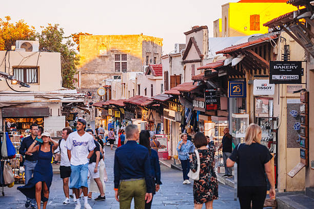 Rhodes, Greece - People walking the busy market street in Rhodes Old Town area at sunset time.