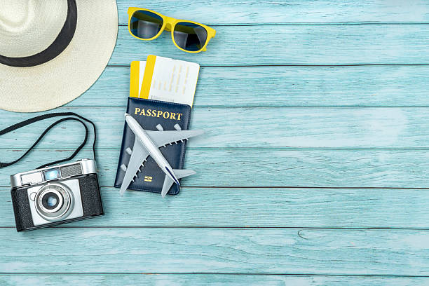 Flat lay of travel accesories composition for summer vacation with passport, boarding passes, airplane, sunglasses, camera and straw hat on light blue wooden background with copy space.