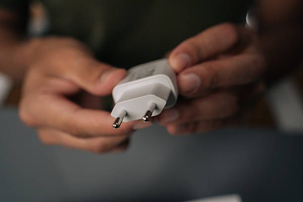 istock Male hands holding checking white charger after unpacking box containing new electronic gadget at table, close-up. 2240650137