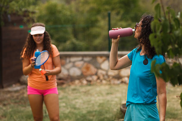 istock Women playing badminton in a tranquil outdoor setting while taking a break to hydrate on a warm day 2240650723