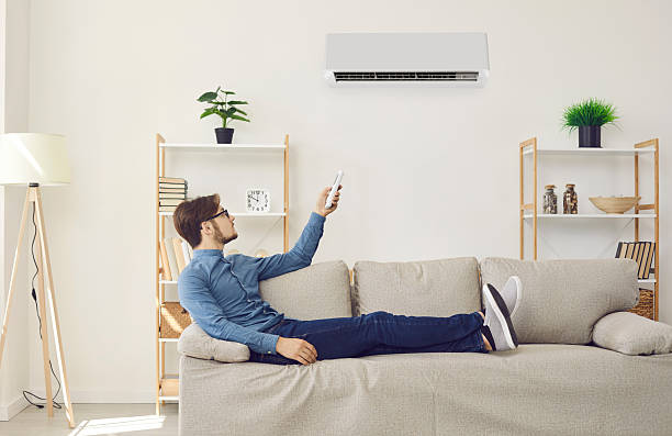 istock Man sitting on couch at home and using remote control to turn on air conditioner 2240651938