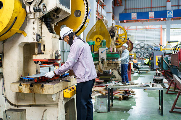 Skilled machine operator or engineer wearing safety uniform and helmet works with a large metal sheet bending and cutting machine inside an industrial factory, demonstrating precision, expertise.
