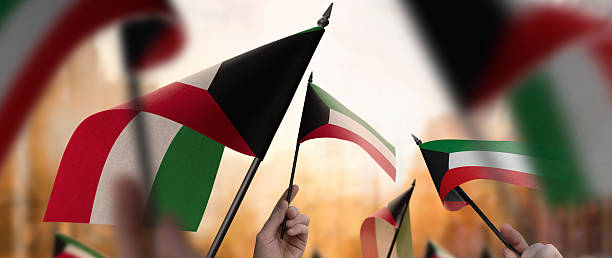 istock Kuwait flags in their hands on a blurred urban background 2240680193