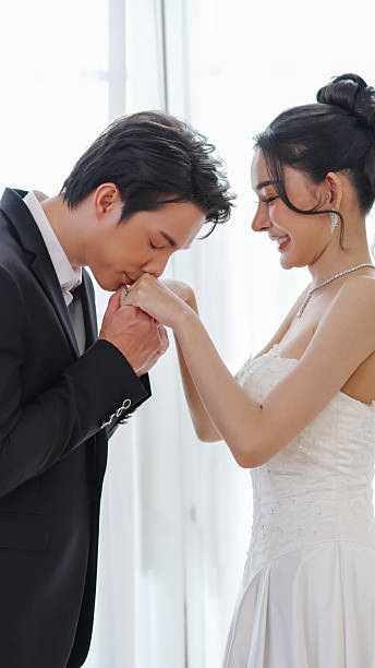 Romantic Gentle Asian groom kissing his bride hand during wedding ceremony, showing love, tenderness, and deep affection in elegant atmosphere.