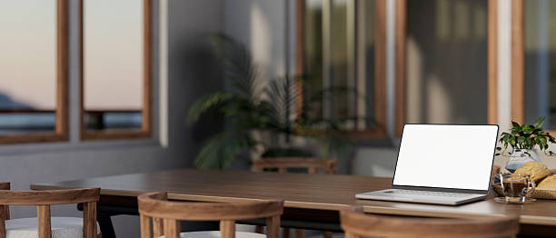istock White screen laptop with breads and coffee cup on table in a dining room with wooden frame windows. 2240682714