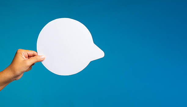 istock Hand holding white speech bubble cutout on blue background. 2240682731