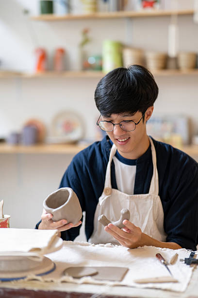 istock Young man potter artist holding handle and clay mug on working table in a pottery class or studio. 2240684080