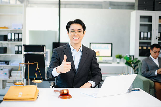 Confident Asian lawyer using tablet with gavel and justice scales on desk, looking at camera. Perfect for law, justice, business, and modern legal technology themes.