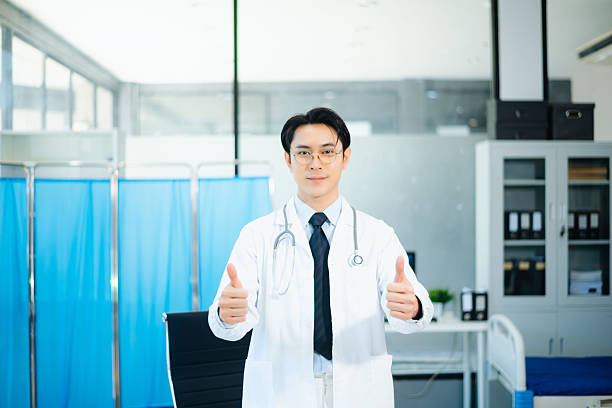 Confident Asian doctor analyzing patient data and looking at camera in modern hospital. Ideal for healthcare, trust, medicine, teamwork, and patient care themes.