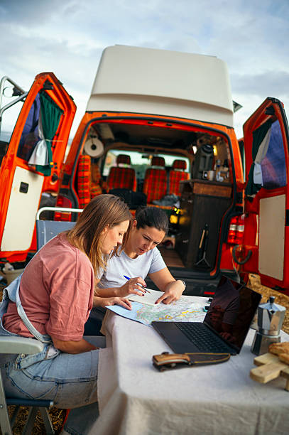 istock Two women planning trip with map and laptop beside orange camper van. 2240684575