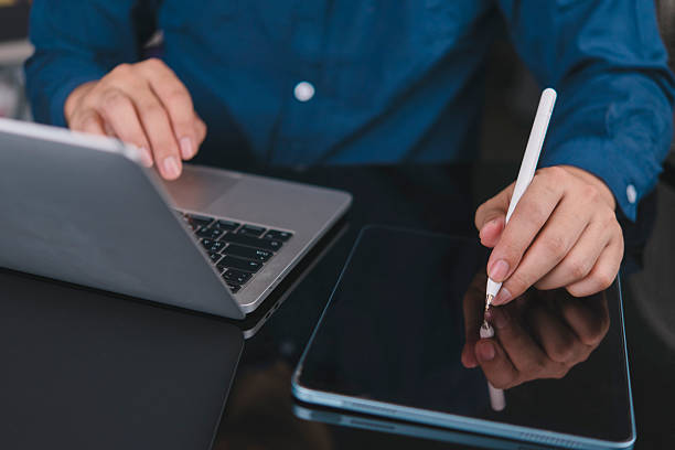 istock Man working remote with laptop and digital tablet. Student learning online, writing notes with stylus. Modern technology for business productivity and multitasking at home office or co-working space. 2240688238