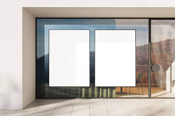 istock Modern glass storefront with two blank vertical poster mockups in black frames reflecting natural landscape outside in minimal architectural setting. 3D Rendering 2240695055