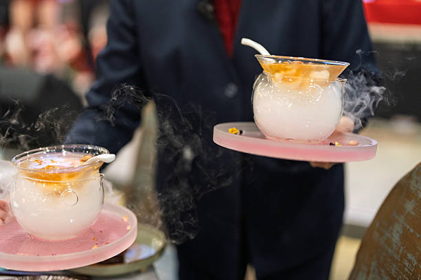 Close-up of a waitress serving traditional Chinese sweet dessert in a glass bowl with dry ice effect during a restaurant dining event.