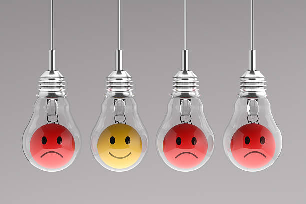 Four light bulbs with emoticons inside, three red and sad and one yellow and happy, hanging from the ceiling